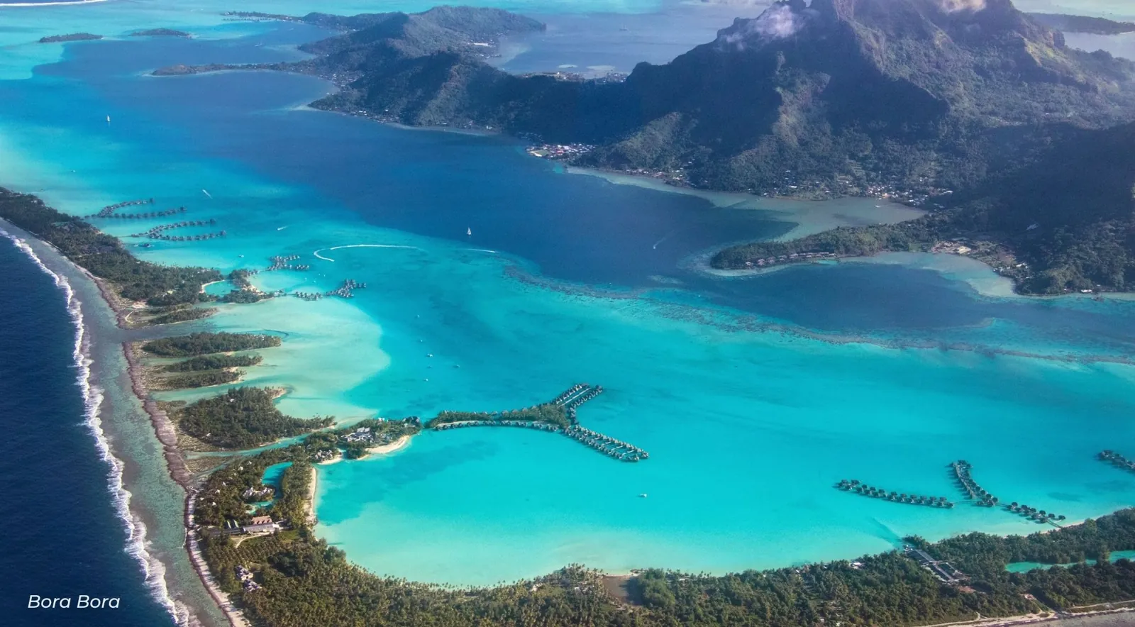 Aerial view of the Bora Bora lagoon, the barrier reef and motus with the main island behind