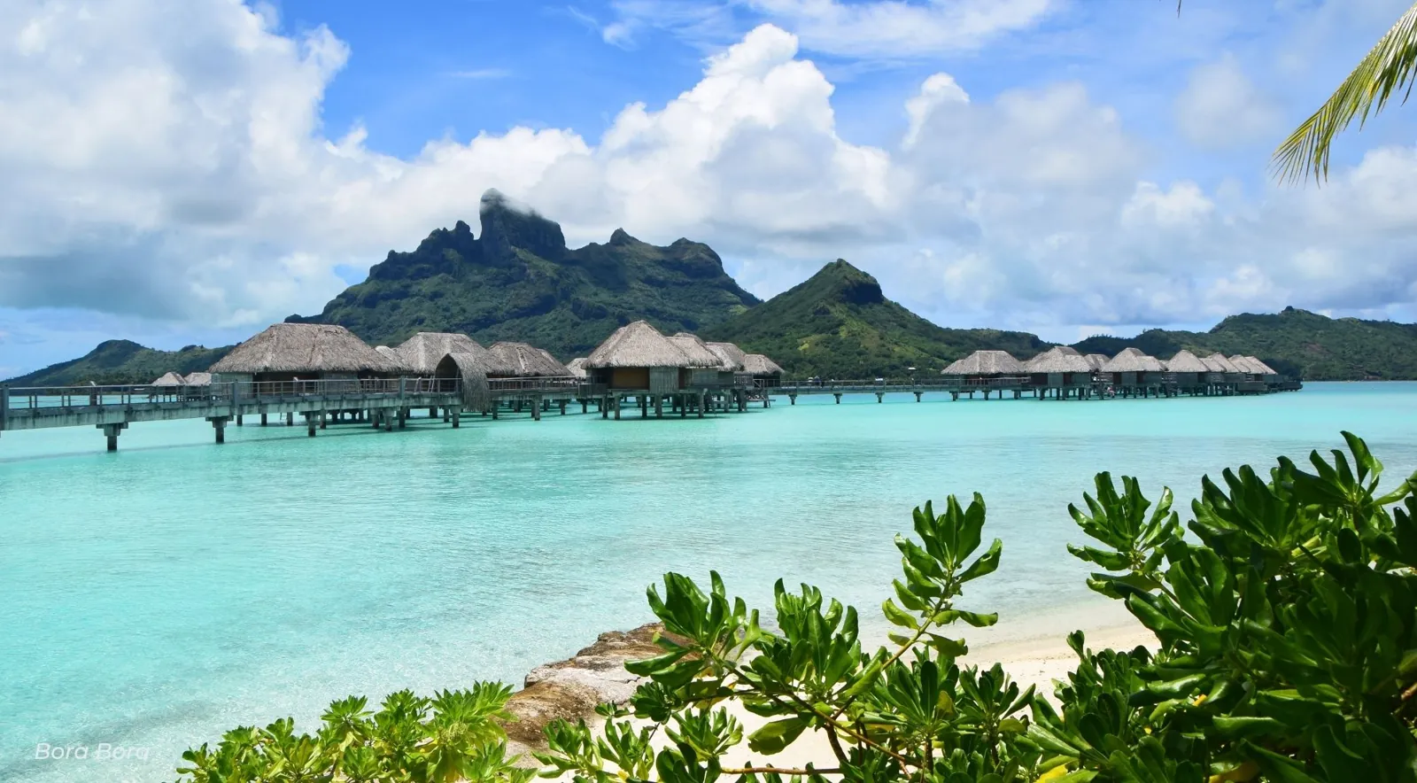 Row of overwater bungalows with the green peaks of Bora Bora behind
